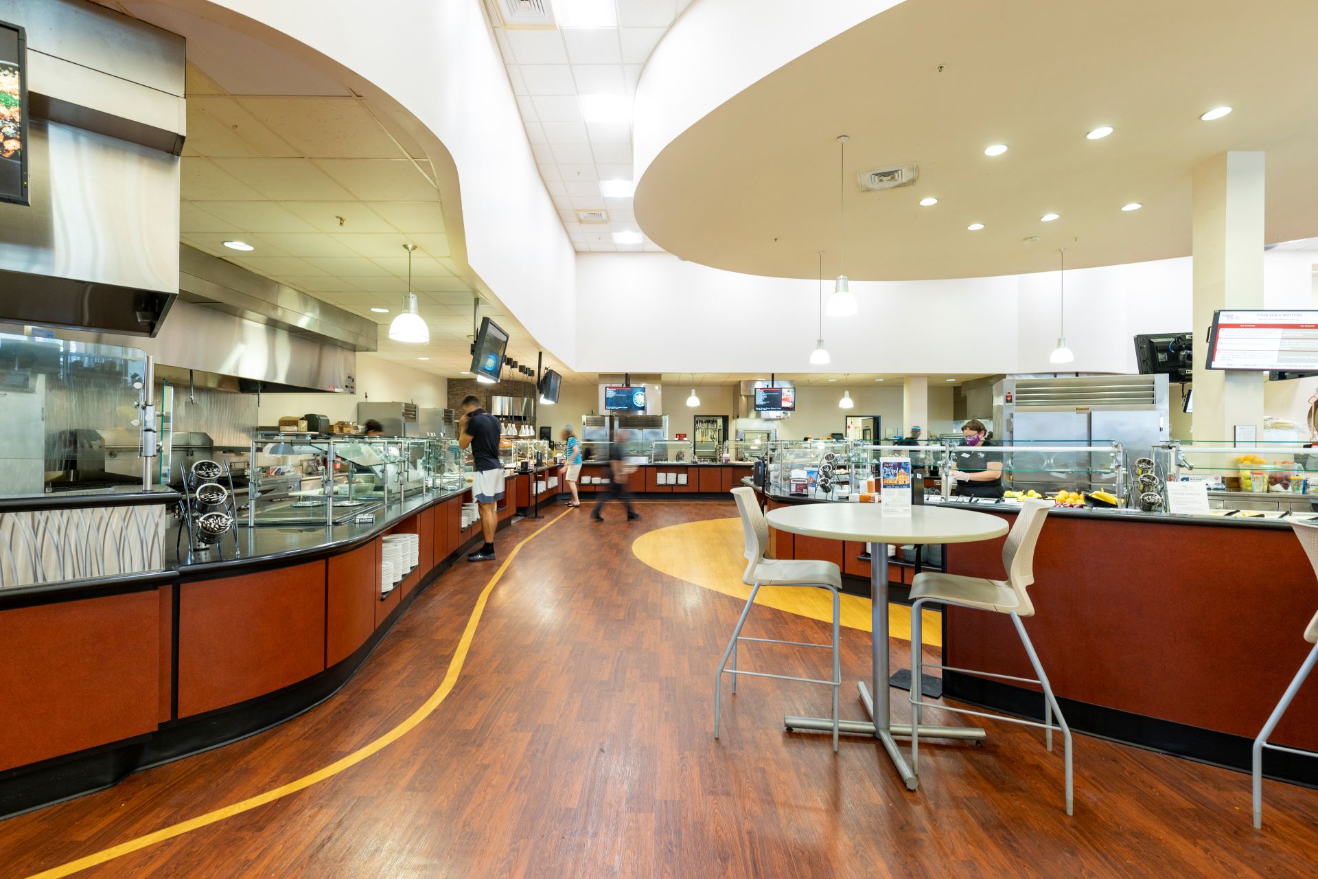 Spacious and modern college dining hall interior with food stations, stainless steel counters, and casual seating areas